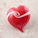 A red heart with a ribbon of white moving from one side to the other with a twist in its center, denoting how two lives come together as one in the heart.